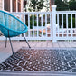 Lifestyle view of black and cream tribal outdoor rug on porch under turquoise chair