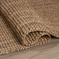 Angled view of natural chunky weave jute area rug rolled on wood floor