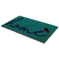 Angled view of non-slip teal coir doormat with cursive navy 'home' and red bird