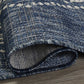 Corner close-up of rolled blue outdoor rug with ivory diamond medallions showing woven back