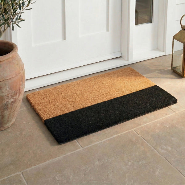 Lifestyle view of natural and black coir doormat at white front door