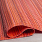 Corner close-up of rolled red and orange striped outdoor rug showing reverse