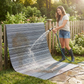 Woman in rubber boots rinsing midnight gray striped outdoor rug with a garden hose
