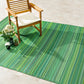Lifestyle view of green striped outdoor rug under wooden armchair with white flowers