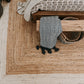 Lifestyle view of natural braided jute area rug with ivory border under bench with gray throw