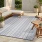 Lifestyle view of light blue and white chevron foldable outdoor rug on patio by wooden sofa