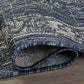 Corner close-up of rolled blue and ivory medallion outdoor rug showing flat weave