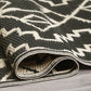 Corner close-up of rolled black and cream tribal outdoor rug showing woven strands