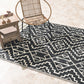Lifestyle view of black and cream tribal outdoor rug under rattan chair and side table