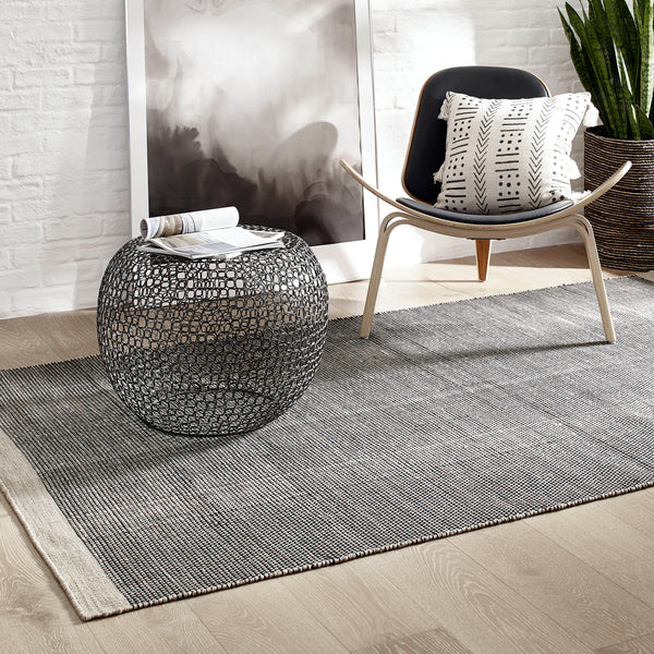 Lifestyle view of black & beige indoor outdoor rug styled on the floor in a room with a pillow on chair