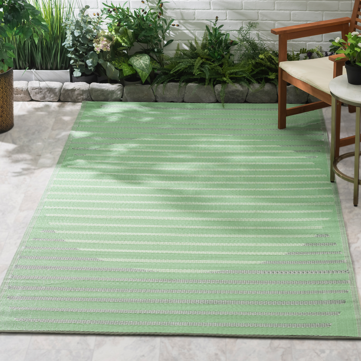 Lifestyle view of green striped circle outdoor rug on patio by wooden armchair