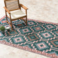 Lifestyle view of green diamond outdoor rug under wooden armchair on stone patio