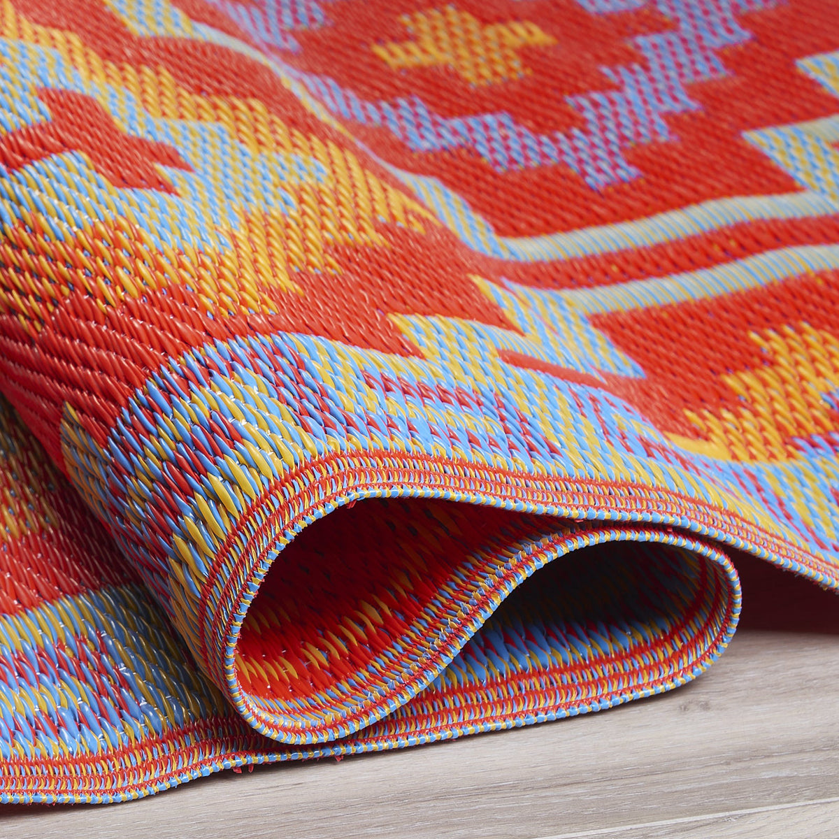 Texture close-up of orange and violet diamond outdoor rug with rolled edge