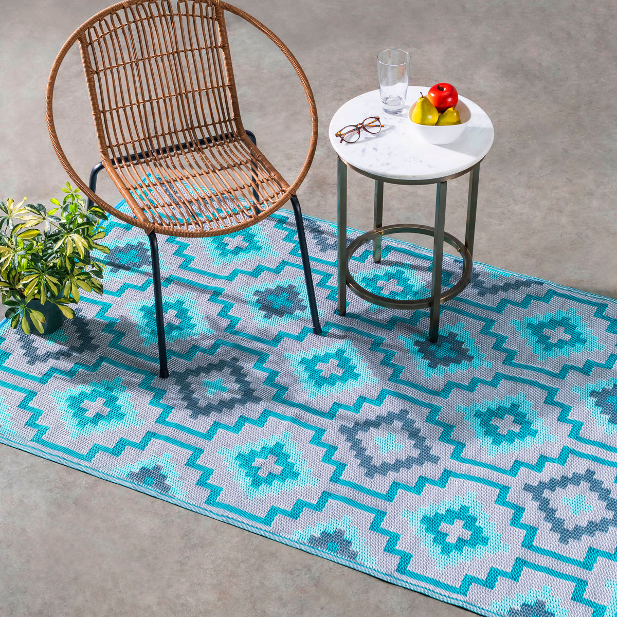 Lifestyle view of teal diamond outdoor rug under rattan chair and marble side table