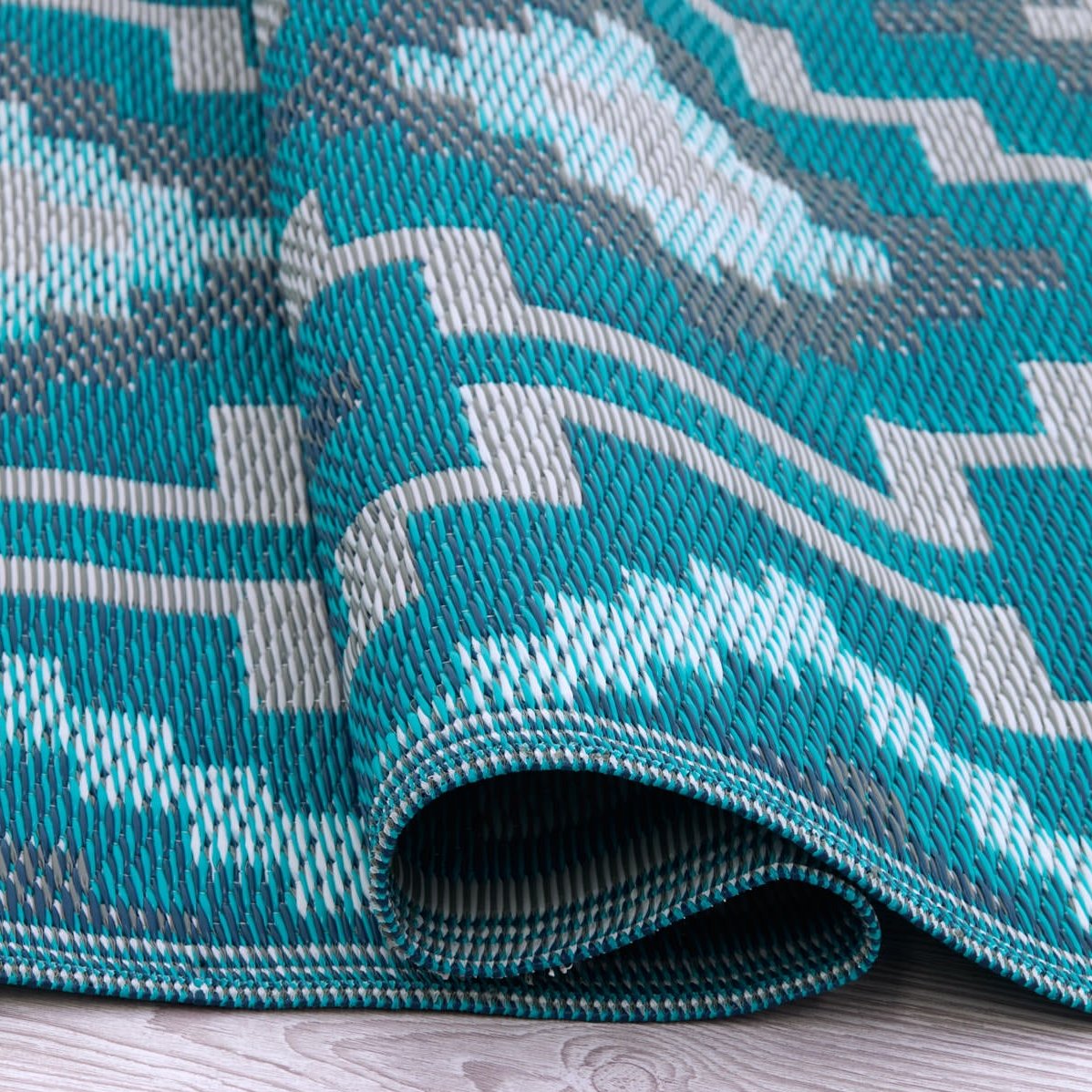 Texture close-up of teal diamond outdoor rug with rolled edge