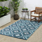 Lifestyle view of teal and gray geometric outdoor rug on patio by wooden armchair