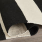 Corner close-up of rolled black and white striped indoor outdoor rug showing reverse