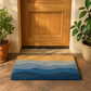 Lifestyle view of blue wave coir doormat at wood front door between potted plants