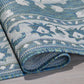 Corner close-up of rolled ocean blue and ivory medallion outdoor rug showing flat weave