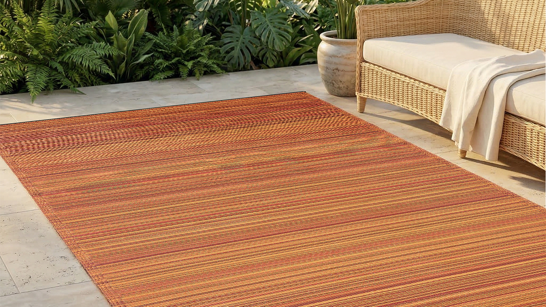 Terracotta striped outdoor rug on a stone patio with a wicker sofa and tropical plants
