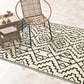 Lifestyle view of black and cream tribal outdoor rug cream side up under rattan chair