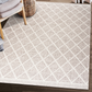 Lifestyle view of beige and ivory lattice machine washable area rug beside woven chair