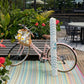 Lifestyle view of rolled outdoor rug in white wave-print carrier bag beside pink bicycle