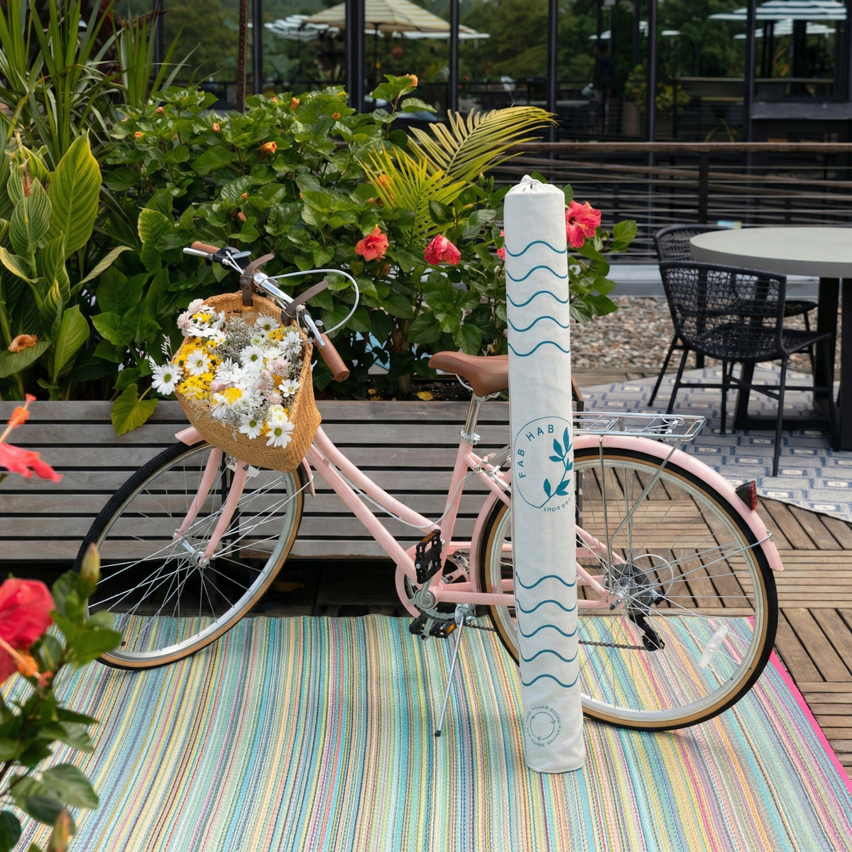 Lifestyle view of rolled outdoor rug in white wave-print carrier bag beside pink bicycle