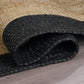 Angled view of natural braided jute area rug with black border rolled on wood floor