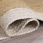 Angled view of natural braided jute area rug with ivory border rolled on wood floor