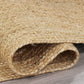 Angled view of natural braided jute area rug rolled on wood floor